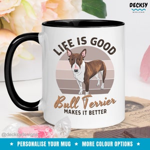May include: White ceramic mug with a black rim and handle. The mug features a brown and white bull terrier dog illustration with a retro sunset background. The text "Life is good Bull Terrier makes it better" is printed on the mug.