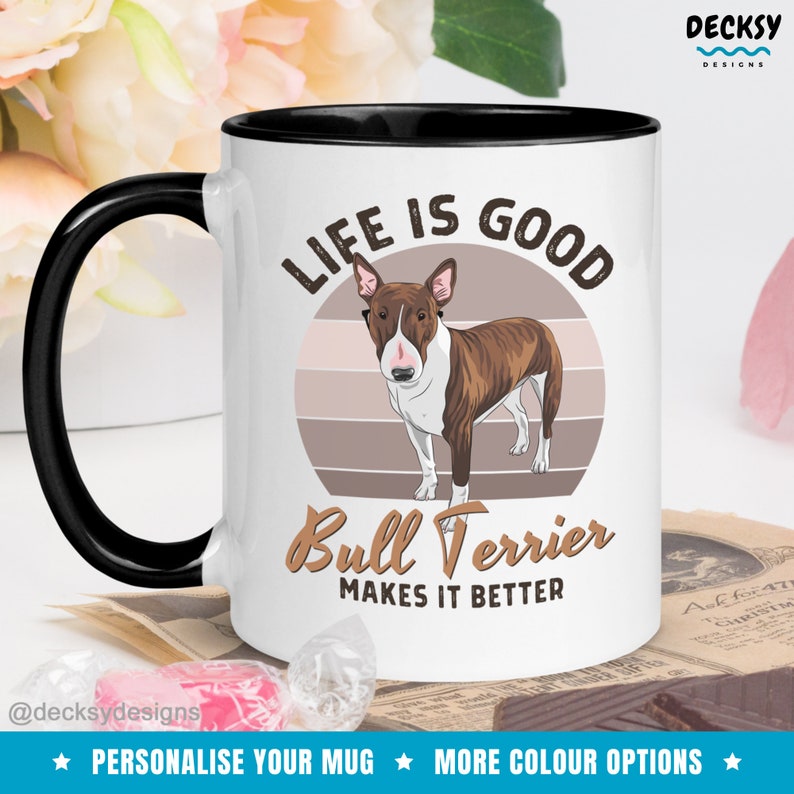 May include: White ceramic mug with a black rim and handle. The mug features a brown and white bull terrier dog illustration with a retro sunset background. The text "Life is good Bull Terrier makes it better" is printed on the mug.