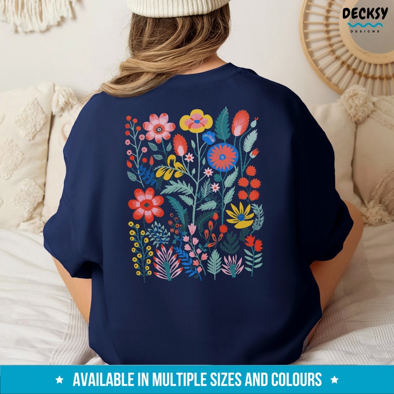 May include: A navy blue sweatshirt with a colorful floral print on the back. The print features a variety of flowers in shades of red, yellow, pink, and blue, with green leaves and stems.