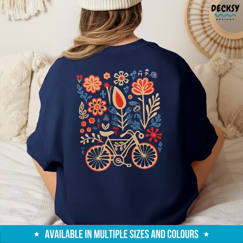 Op de afbeelding: Donkerblauw sweatshirt met een kleurrijk bloemenontwerp en een fiets in het midden. Het ontwerp bevat rode, oranje, gele, blauwe en groene bloemen.