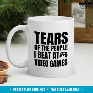 May include: White ceramic mug with black text that reads "Tears of the people I beat at video games" and a black video game controller icon.