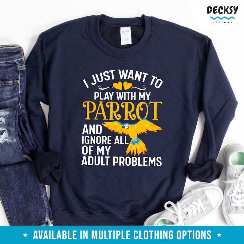 May include: A navy blue sweatshirt with the text "I just want to play with my parrot and ignore all of my adult problems". A yellow parrot with a blue head is flying above the text. The text is in white and the background is navy blue.