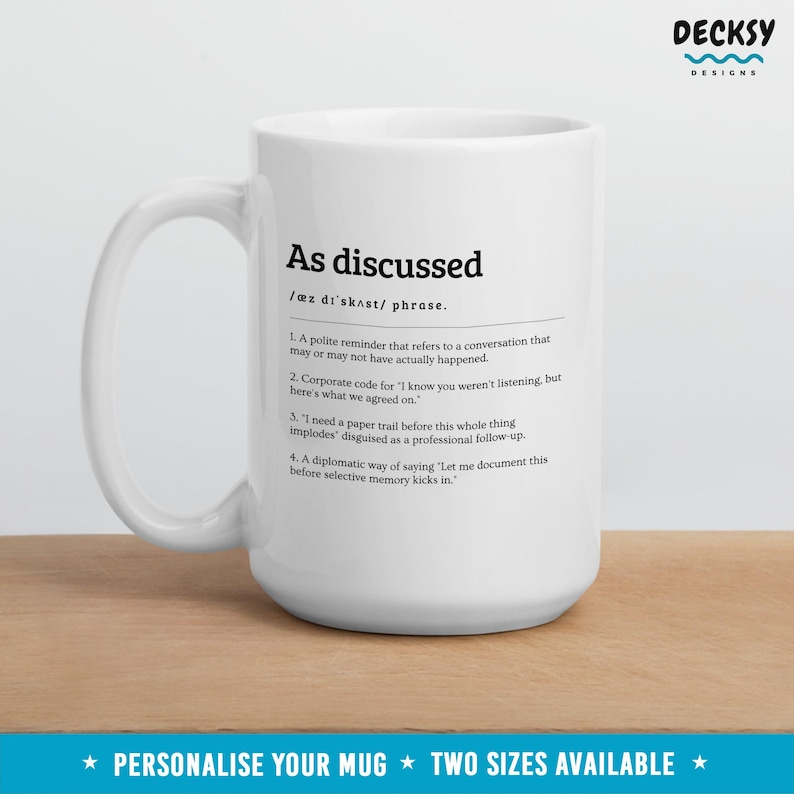 Peut inclure: Un mug en c&eacute;ramique blanc avec l'expression "As discussed" imprim&eacute;e en noir, accompagn&eacute;e d'une d&eacute;finition. Le mug pr&eacute;sente &eacute;galement le texte "Personalise your mug" et "Two sizes available". Le mug est pos&eacute; sur une surface en bois.