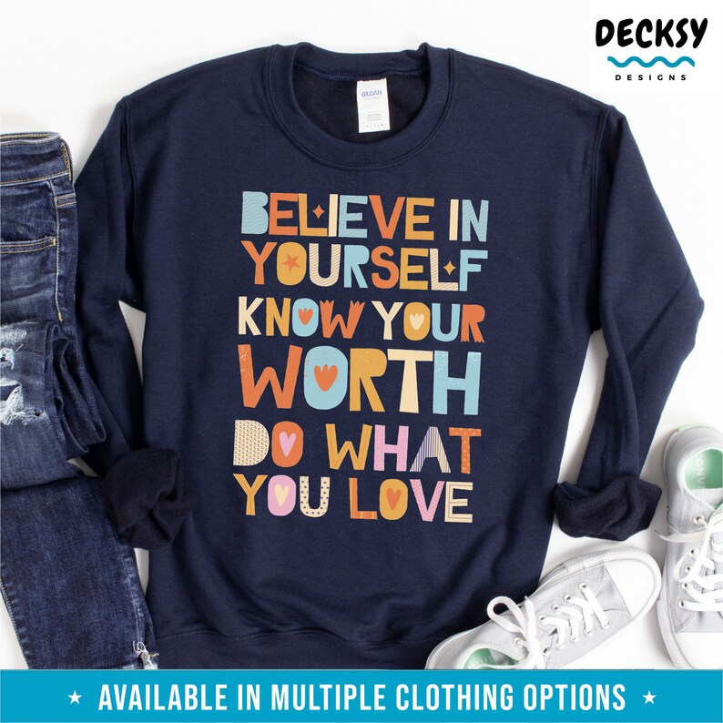 K&ouml;nnte beinhalten: Marineblaues Sweatshirt mit dem Text "BELIEVE IN YOURSELF KNOW YOUR WORTH DO WHAT YOU LOVE" in farbenfrohen, verspielten Buchstaben. Das Sweatshirt wird mit blauen Jeans und grauen Turnschuhen kombiniert. Das Design enth&auml;lt einen Stern und ein Herz.