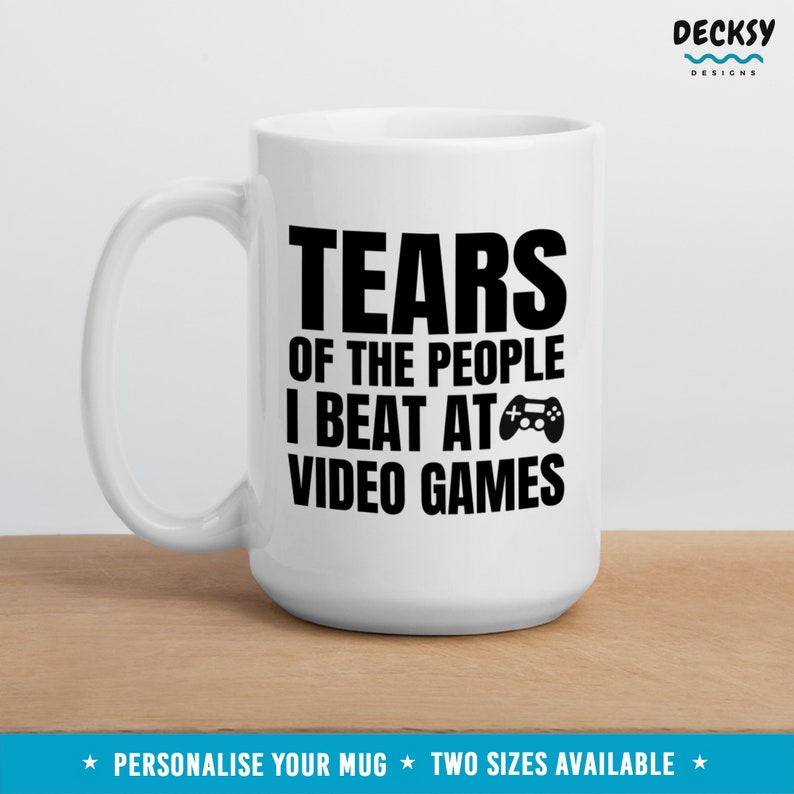 May include: White ceramic mug with a black graphic that reads "Tears of the people I beat at video games" and a black video game controller icon.