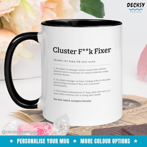Puede incluir: Taza de café de cerámica blanca con borde y asa negros. La taza presenta una definición humorística del término "Cluster F**k Fixer" en texto negro.