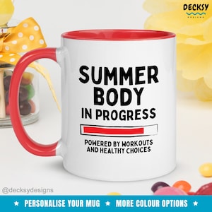 Może przedstawiać: Biały kubek ceramiczny z czerwonym rantem i uchwytem. Kubek ma czarny napis "SUMMER BODY IN PROGRESS" z czerwonym paskiem postępu poniżej. Napis "POWERED BY WORKOUTS AND HEALTHY CHOICES" znajduje się pod paskiem postępu.