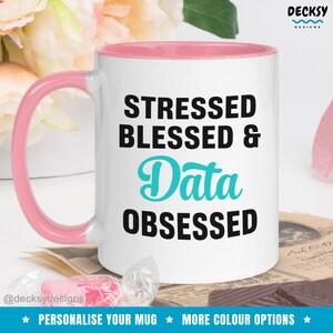 May include: White ceramic mug with a pink rim and handle. The mug has black text that reads "Stressed Blessed & Data Obsessed". The word "Data" is in turquoise.