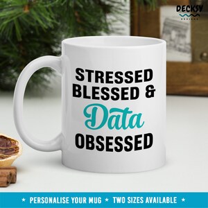 May include: White ceramic mug with a black and teal design. The text on the mug reads "Stressed Blessed & Data Obsessed".