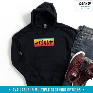 May include: Black hooded sweatshirt with a graphic of the evolution of man culminating in a surfer riding a wave. The graphic is set against a colorful striped background.