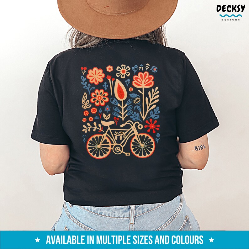 Op de afbeelding: Zwart T-shirt met een kleurrijk bloemenontwerp en een fiets in het midden. Het ontwerp bevat rode, oranje, gele, blauwe en groene bloemen. De tekst "Girl" is gedrukt op de rechtermouw.