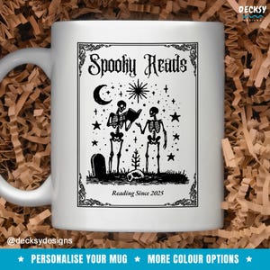 Op de afbeelding: Witte keramische mok met een zwart-wit ontwerp. De mok heeft de tekst "Spooky Reads" en een illustratie van twee skeletten die boeken lezen, een halve maan, sterren en een grafsteen. De tekst "Reading Since 2025" is ook inbegrepen.