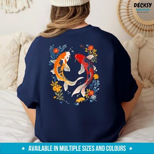 May include: A navy blue t-shirt featuring a design of two koi fish swimming in a circle surrounded by flowers. The fish are orange, red, and white.