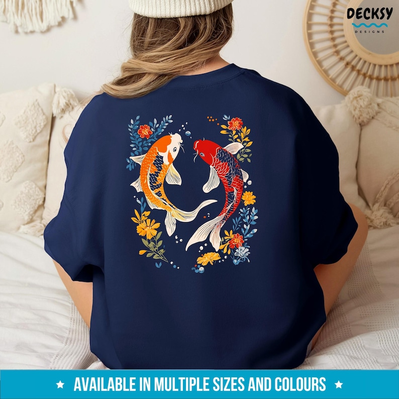 May include: A navy blue t-shirt featuring a design of two koi fish swimming in a circle surrounded by flowers. The fish are orange, red, and white.