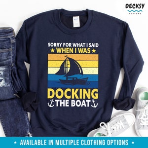 May include: Navy blue sweatshirt with a vintage-style graphic of a sailboat and the text "Sorry for what I said when I was docking the boat".
