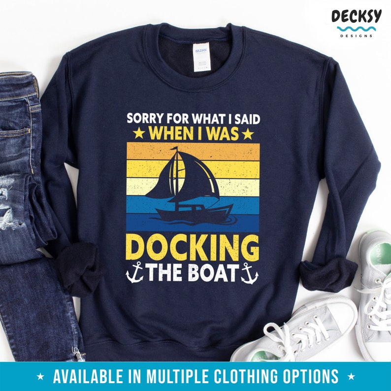 May include: Navy blue sweatshirt with a vintage-style graphic of a sailboat and the text "Sorry for what I said when I was docking the boat".