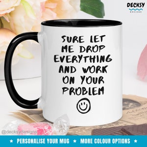 Op de afbeelding: Witte keramische mok met een zwarte rand en handvat. De mok heeft zwarte tekst die "Sure let me drop everything and work on your problem" luidt met een smiley onder de tekst.