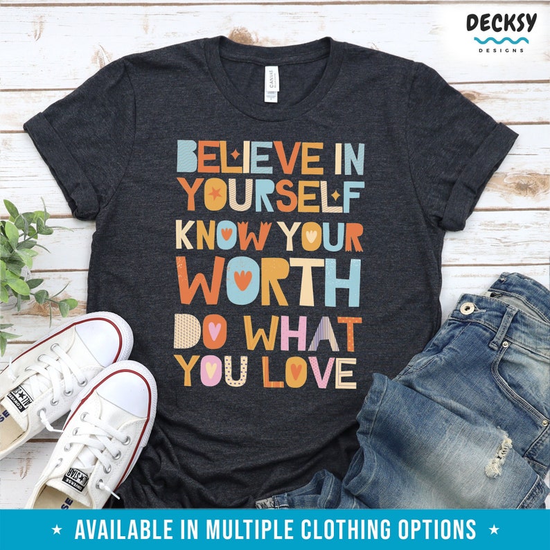 K&ouml;nnte beinhalten: Dunkelgraues T-Shirt mit dem Text "BELIEVE IN YOURSELF KNOW YOUR WORTH DO WHAT YOU LOVE" in bunten Blockbuchstaben. Wei&szlig;e Leinenschuhe und blaue Jeans sind ebenfalls im Bild. Der Text "AVAILABLE IN MULTIPLE CLOTHING OPTIONS" befindet sich unten.