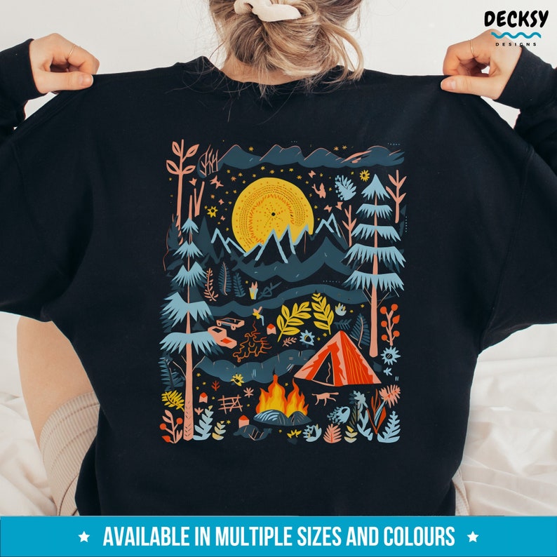 May include: A black sweatshirt with a colorful illustration of a camping scene. The design features a campfire, a tent, a car, trees, and a full moon. The text "AVAILABLE IN MULTIPLE SIZES AND COLORS" is printed below the design.
