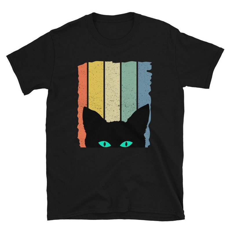 May include: Black t-shirt with a retro-style design of a cat peeking out from behind colorful stripes. The cat has green eyes.