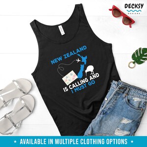May include: Black tank top with a blue graphic of New Zealand, a kiwi bird, and an airplane. The text "New Zealand is calling and I must go" is printed on the shirt.