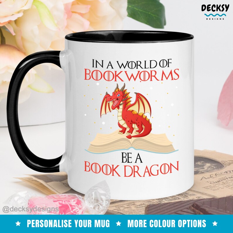 May include: White ceramic mug with a black rim and handle. The mug features a red dragon sitting on an open book with the text "In a world of bookworms be a book dragon".