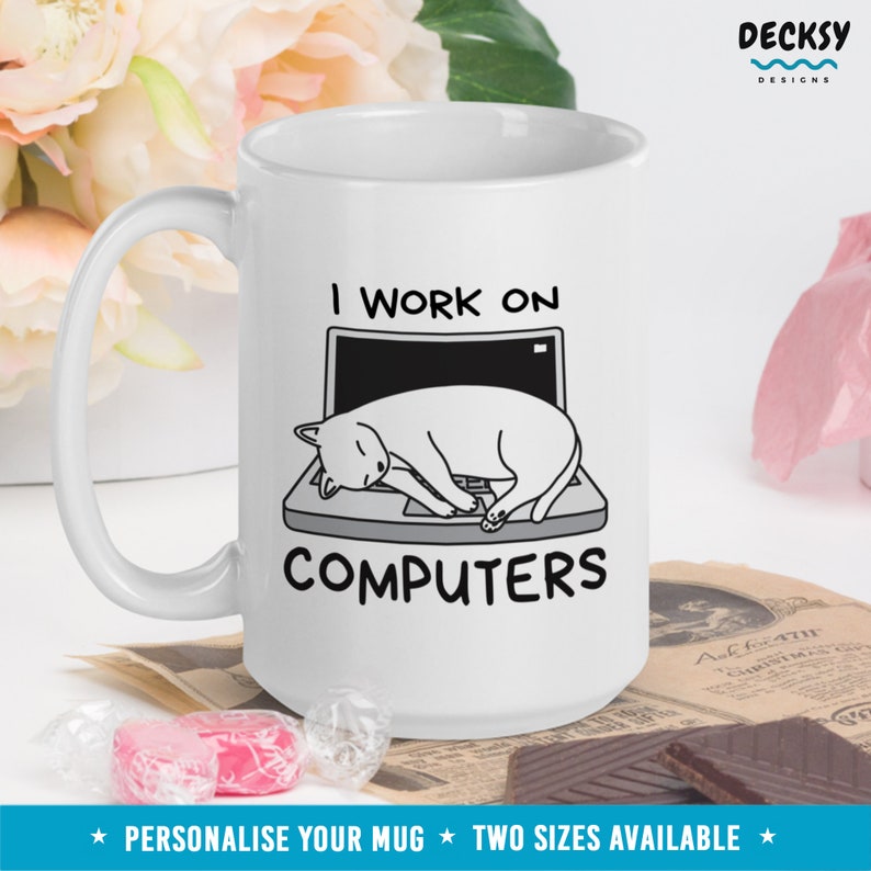 May include: White ceramic mug with a black outline of a cat sleeping on a laptop. The text "I work on computers" is printed on the mug.