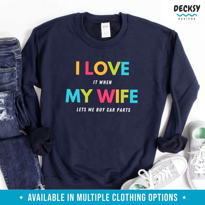 Pu&ograve; includere: Felpa blu navy con la scritta "I LOVE IT WHEN MY WIFE LETS ME BUY CAR PARTS" a blocchi colorati. La felpa &egrave; esposta con un paio di jeans e scarpe da ginnastica.