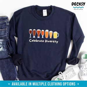 May include: A navy blue sweatshirt featuring a graphic of different beer glasses in shades of brown and yellow. The white text "Celebrate Diversity" is printed below. The sweatshirt is shown with jeans and trainers.