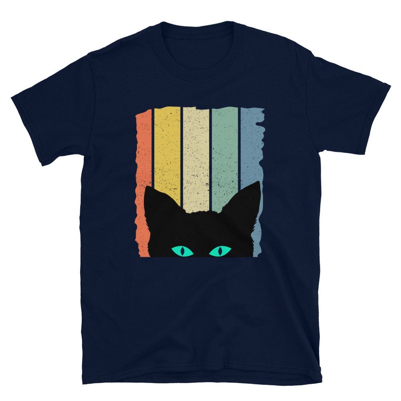 May include: A navy blue t-shirt with a retro-style graphic of a black cat peeking out from behind colorful stripes. The cat has bright green eyes.