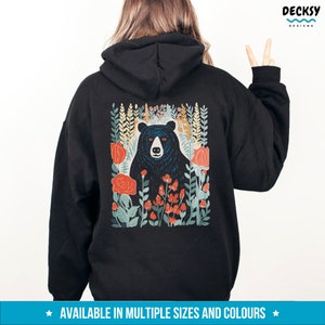 May include: Black hoodie with a graphic print of a black bear surrounded by colorful flowers. The bear is looking directly at the viewer. The text "AVAILABLE IN MULTIPLE SIZES AND COLORS" is printed at the bottom of the image.