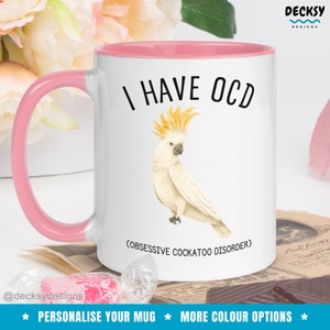 Puede incluir: Taza de cer&aacute;mica blanca con borde y asa de color rosa. La taza presenta un cacat&uacute;a blanco con cresta amarilla y el texto "TENGO TOC (TRASTORNO OBSESIVO COMPULSIVO)".