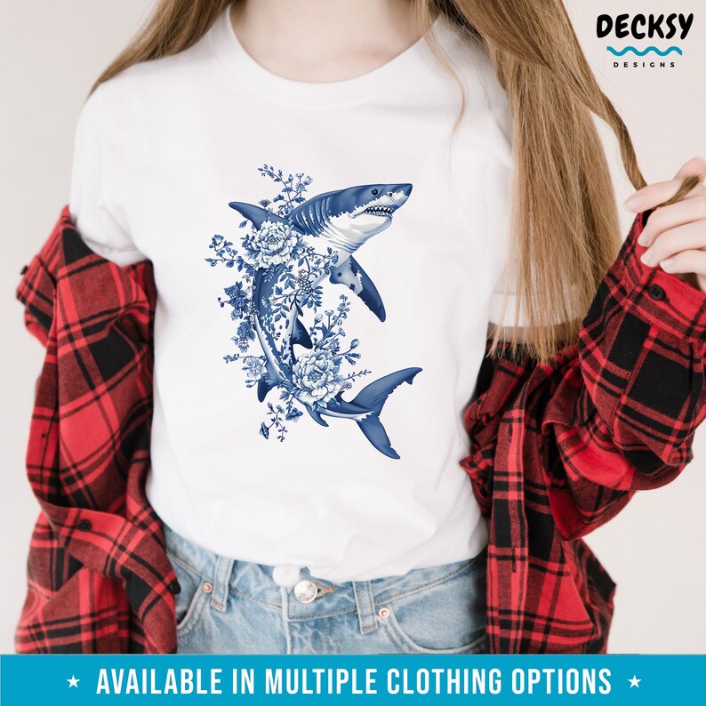 Puede incluir: Camiseta blanca con un gr&aacute;fico azul y blanco de un tibur&oacute;n con detalles florales. El tibur&oacute;n est&aacute; nadando hacia arriba con la boca abierta. Los detalles florales son de estilo porcelana azul y blanco.