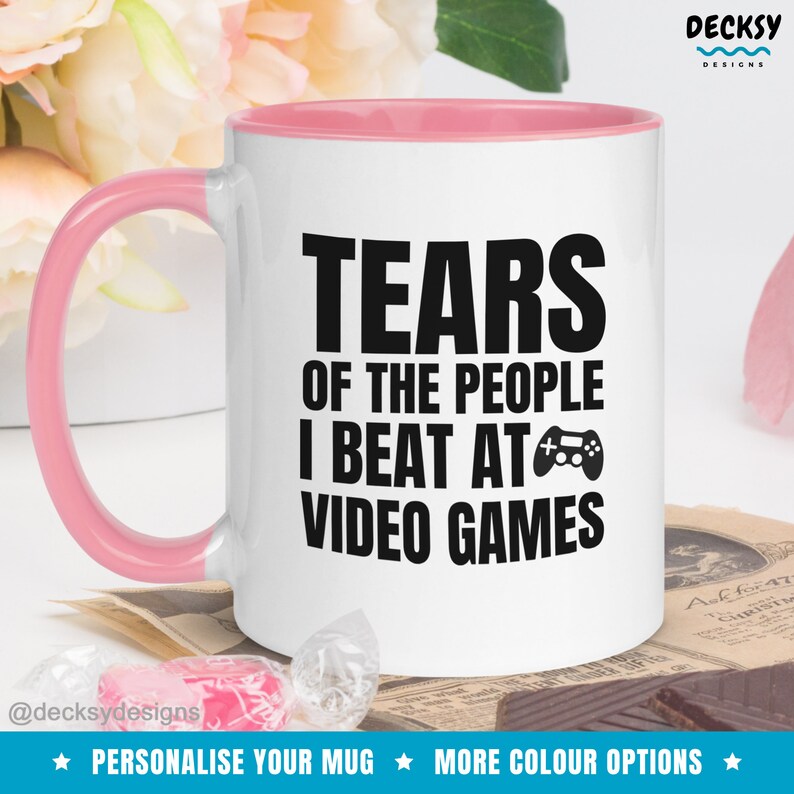 May include: White ceramic mug with a pink rim and handle. The mug has black text that reads "Tears of the people I beat at video games" with a video game controller icon.