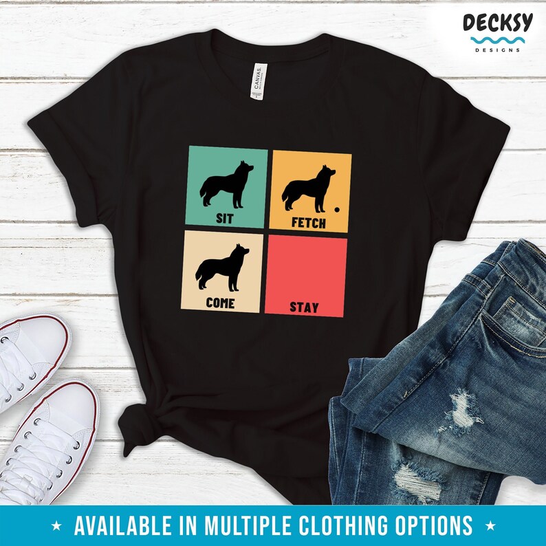 Op de afbeelding: Zwart T-shirt met een retro ontwerp met vier silhouetten van een husky-hond met de woorden "Sit", "Fetch", "Come" en "Stay" in een rasterpatroon.