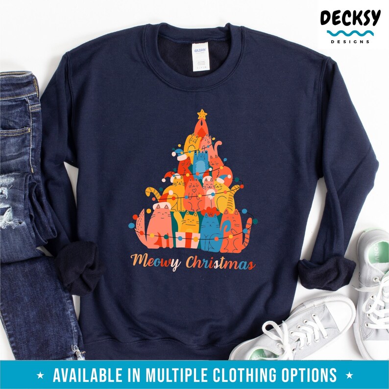May include: A navy blue sweatshirt with a Christmas tree design made of cats. The cats are wearing Santa hats and are decorated with Christmas lights. The text "Meowy Christmas" is printed below the tree.