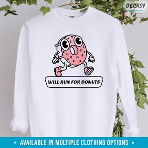 Puede incluir: Sudadera blanca con un dibujo animado de donut rosa y negro corriendo y el texto "WILL RUN FOR DONUTS".