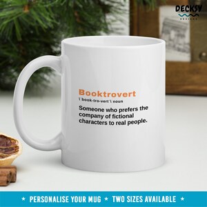May include: White ceramic mug with a black and orange design. The mug features the word "Booktrovert" defined as "Someone who prefers the company of fictional characters to real people."