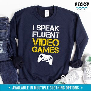 May include: A navy blue sweatshirt with a yellow graphic that says "I speak fluent video games" and a white video game controller graphic.