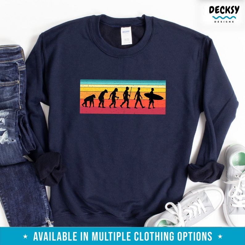 May include: A navy blue sweatshirt with a vintage-style graphic of the evolution of man, culminating in a surfer holding a surfboard. The graphic is set against a colorful striped background.