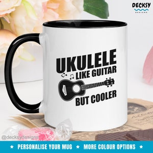 May include: White ceramic mug with a black rim and handle. The mug features a black and white illustration of a ukulele with the text "Ukulele Like Guitar But Cooler".