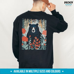 May include: Black sweatshirt with a graphic print of a black bear in a forest setting with red flowers. The text "DECKSY DESIGNS" is in the upper right corner of the image.