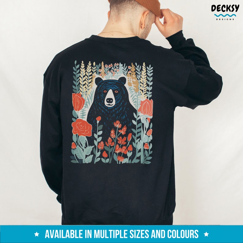 May include: Black sweatshirt with a graphic print of a black bear in a forest setting with red flowers. The text "DECKSY DESIGNS" is in the upper right corner of the image.