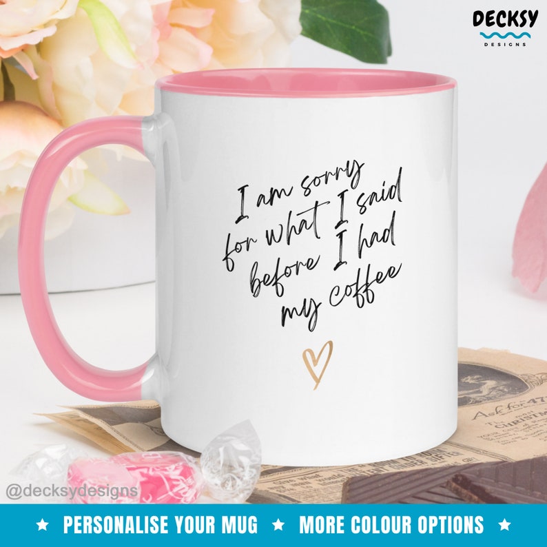 May include: White ceramic coffee mug with a pink rim and handle. The mug has black text that reads "I am sorry for what I said before I had my coffee" with a gold heart below the text.