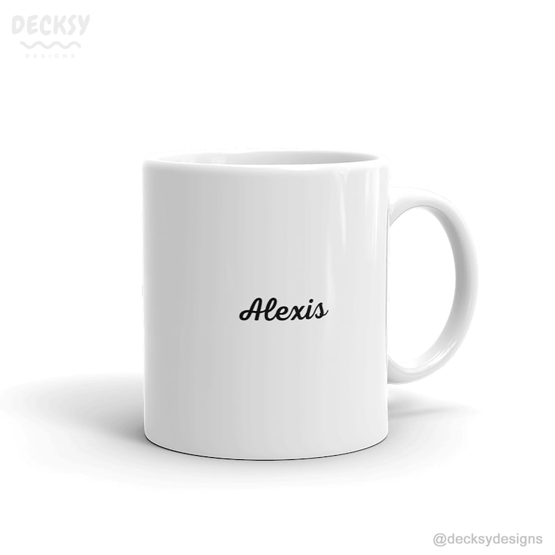 K&ouml;nnte beinhalten: Eine wei&szlig;e Keramiktasse mit einer schwarzen, kursiv geschriebenen Aufschrift "Alexis".