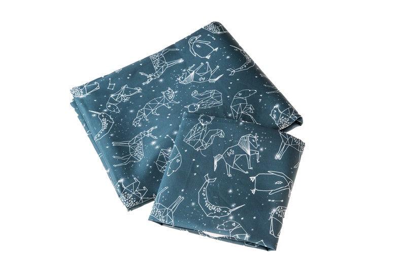 May include: Two folded teal fabric pieces with a white geometric animal constellation pattern. The design includes a fox, bear, narwhal, and horse. The fabric has a starry night sky background.