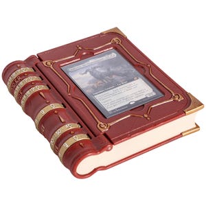 May include: A burgundy-colored card holder shaped like a book, with gold accents and a combination lock on the spine. The open book displays a card with a fantasy illustration. The card holder is designed to protect and store collectible cards.