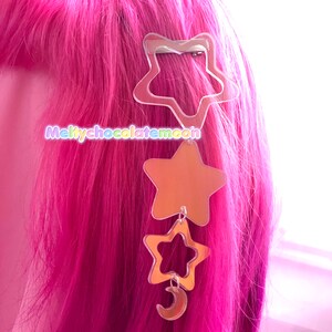 Puede incluir: Una pinza para el pelo en forma de estrella plateada con una cadena colgante de tres estrellas m&aacute;s peque&ntilde;as y una luna creciente. Las estrellas son de espejo y la luna es de espejo.