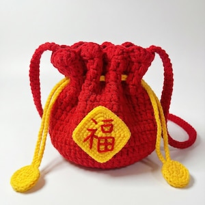 May include: A handmade red crochet pouch with yellow drawstrings and a yellow square patch with Chinese characters. The pouch has a drawstring closure and two red crochet handles. The overall design is a vibrant red and yellow color scheme.
