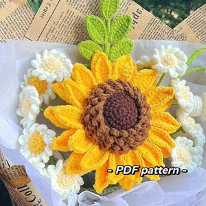 Puede incluir: Un ramo de girasoles y margaritas de ganchillo. El girasol es amarillo con un centro marrón. Las margaritas son blancas con centros amarillos. El ramo está envuelto en papel de seda blanco y atado con una cinta marrón. - PDF pattern -